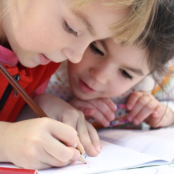 Das Foto zeigt zwei Mädchen beim Schreiben / Malen mit einem Bleistift.