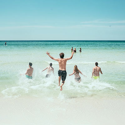 Das Bild zeigt fünf Jugendliche, die ins Meer laufen.