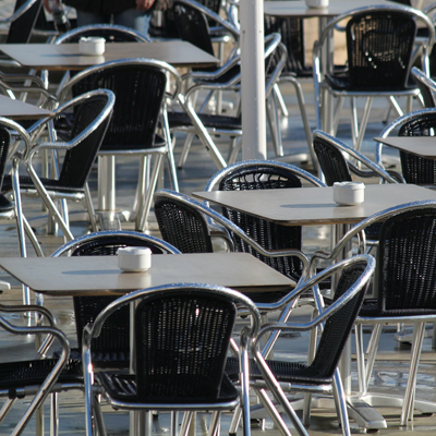 Das Foto zeigt einen Ausschnitt einer Außengastronomie. Es sind Tische und Stühle zu erkennen.