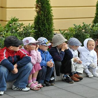 Das Bild zeigt sechs Kinder, die vor einem Zaun sitzen.